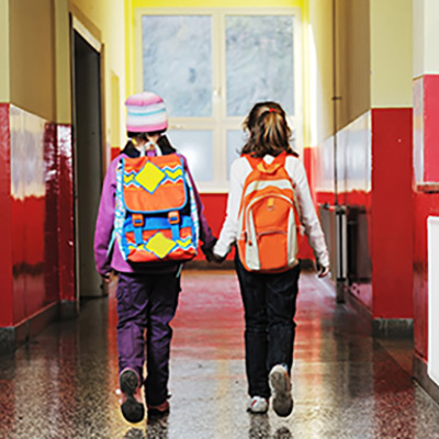 Two little girls holding hands walking down a school hallway