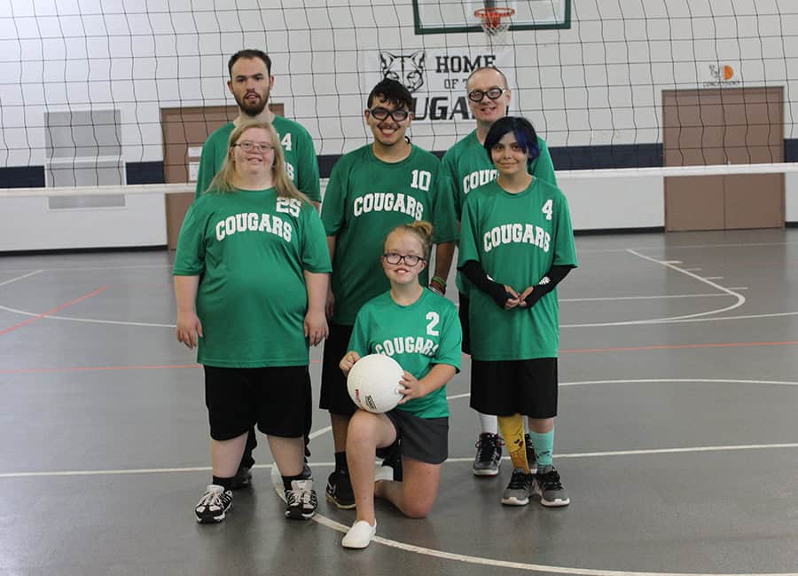 Group of Special Olympics athletes in green jerseys on indoor basketball court.