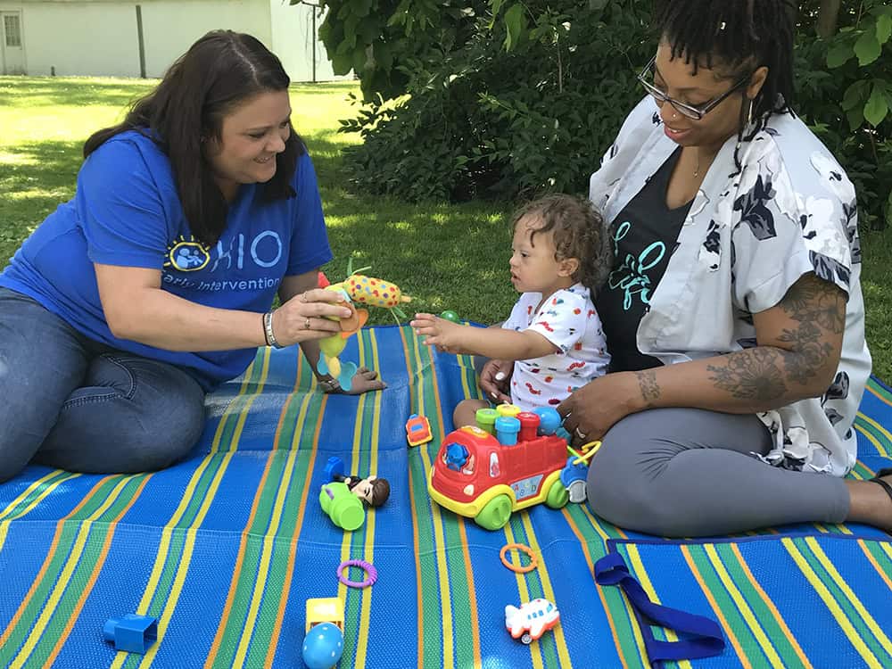 Two women playing with a small toddler on a blanket