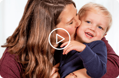 Woman hugging a smiling young child with developmental disabilities.